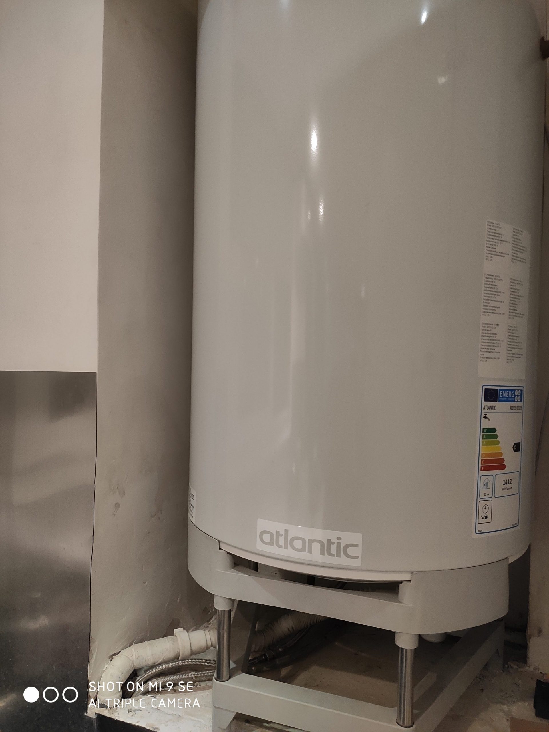 Chauffe-eau vertical blanc posé sur un socle, avec l'étiquette « atlantic » et une étiquette énergie, dans un local technique.