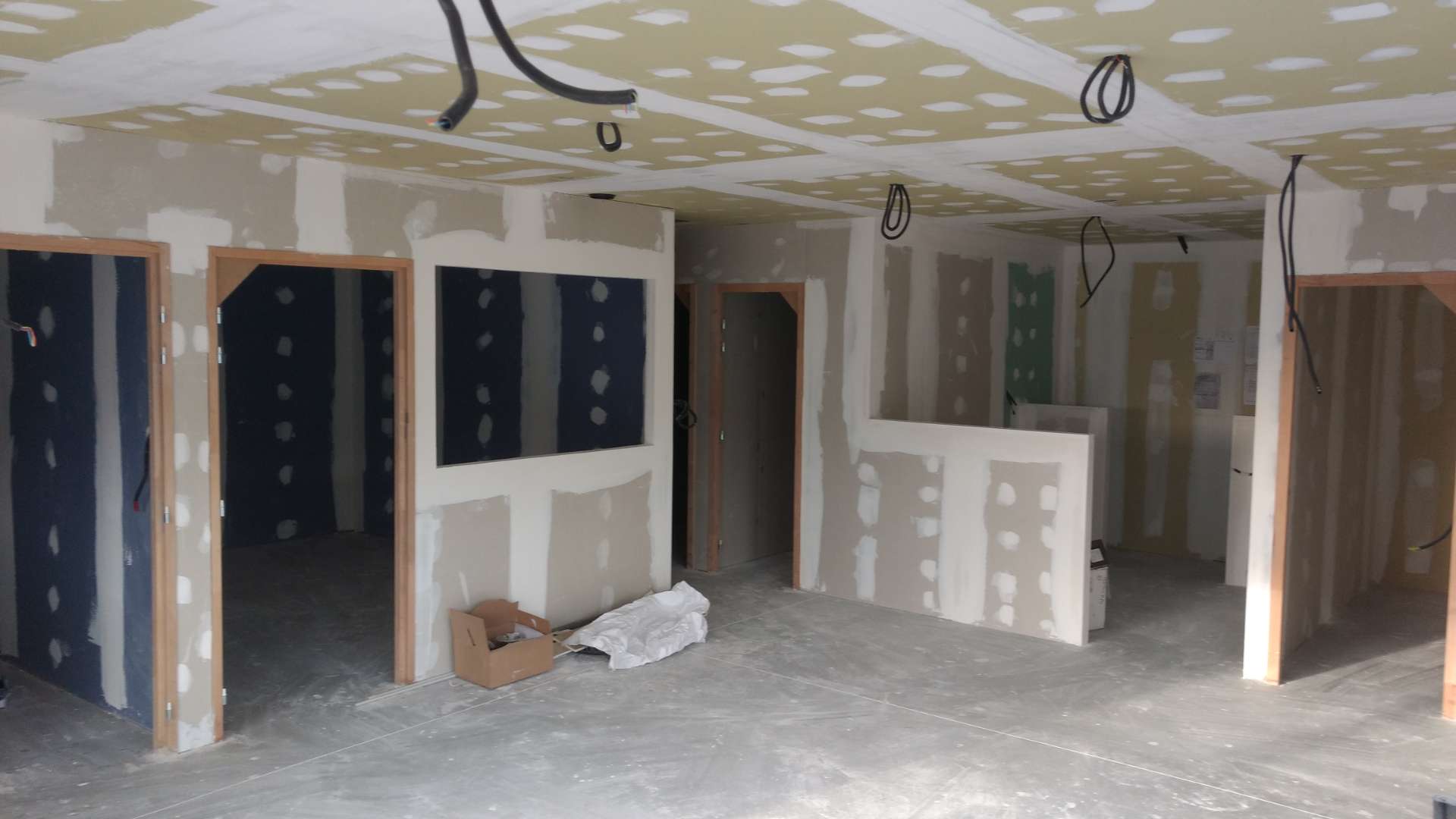 Pièce en travaux avec cloisons en plaques de plâtre, ouvertures de portes sans portes, câbles électriques pendant du plafond et carton au sol.